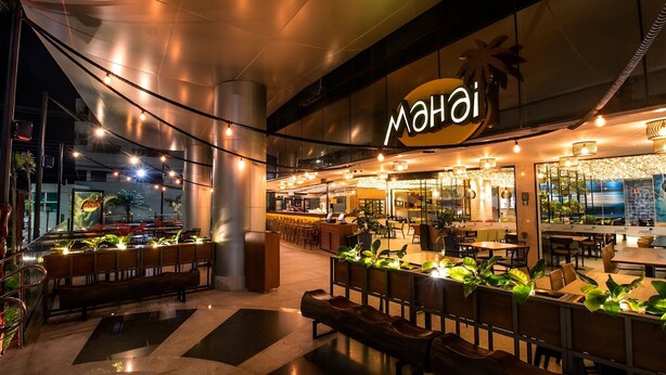 En restaurang med en skylt som visar ordet ”Maho”, uteservering med växter och en modern inredning.