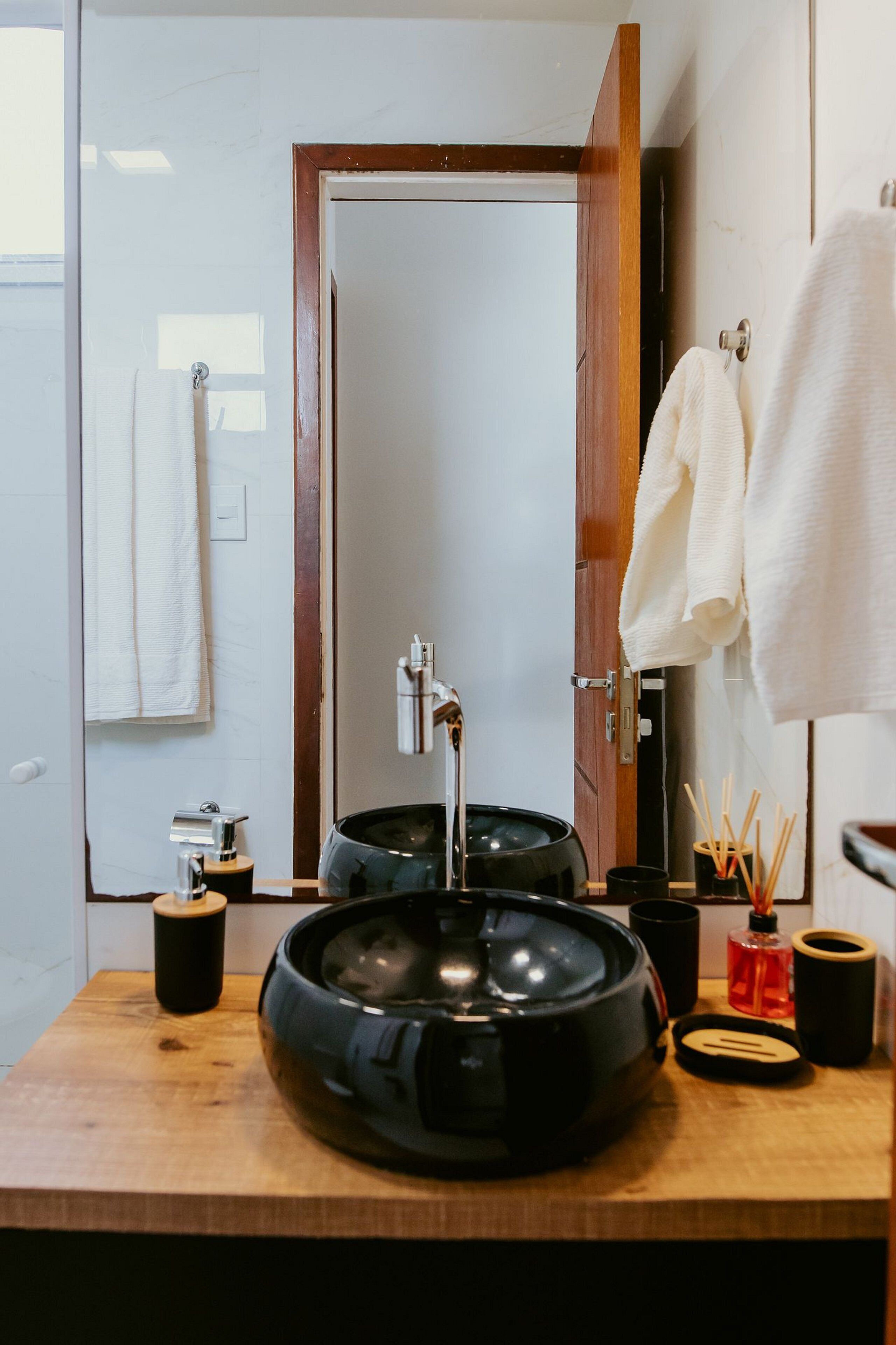 A bathroom with a wooden vanity, a black sink, a mirror, and a towel rack.