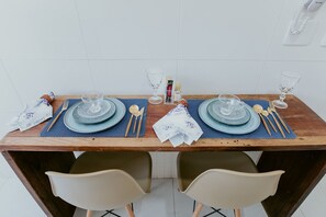 Ein Esstisch ist gedeckt mit blauen Tellern, klaren Gläsern und Essstäbchen, und an der Wand hängt ein Telefon.