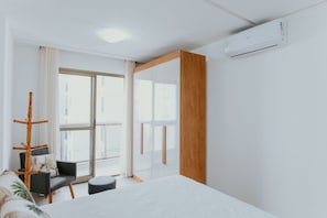 Ein modernes Schlafzimmer mit Bett, Sessel, Fenster und Klimaanlage.