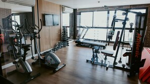 Un gimnasio con equipo de ejercicio, cinta de correr y pared espejada.