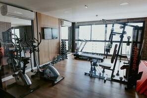 Academia com equipamentos de ginástica, esteira e espelho.