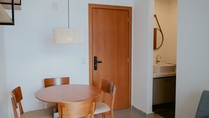 Un comedor con una mesa redonda y sillas, una puerta de madera y una kitchenette al fondo.