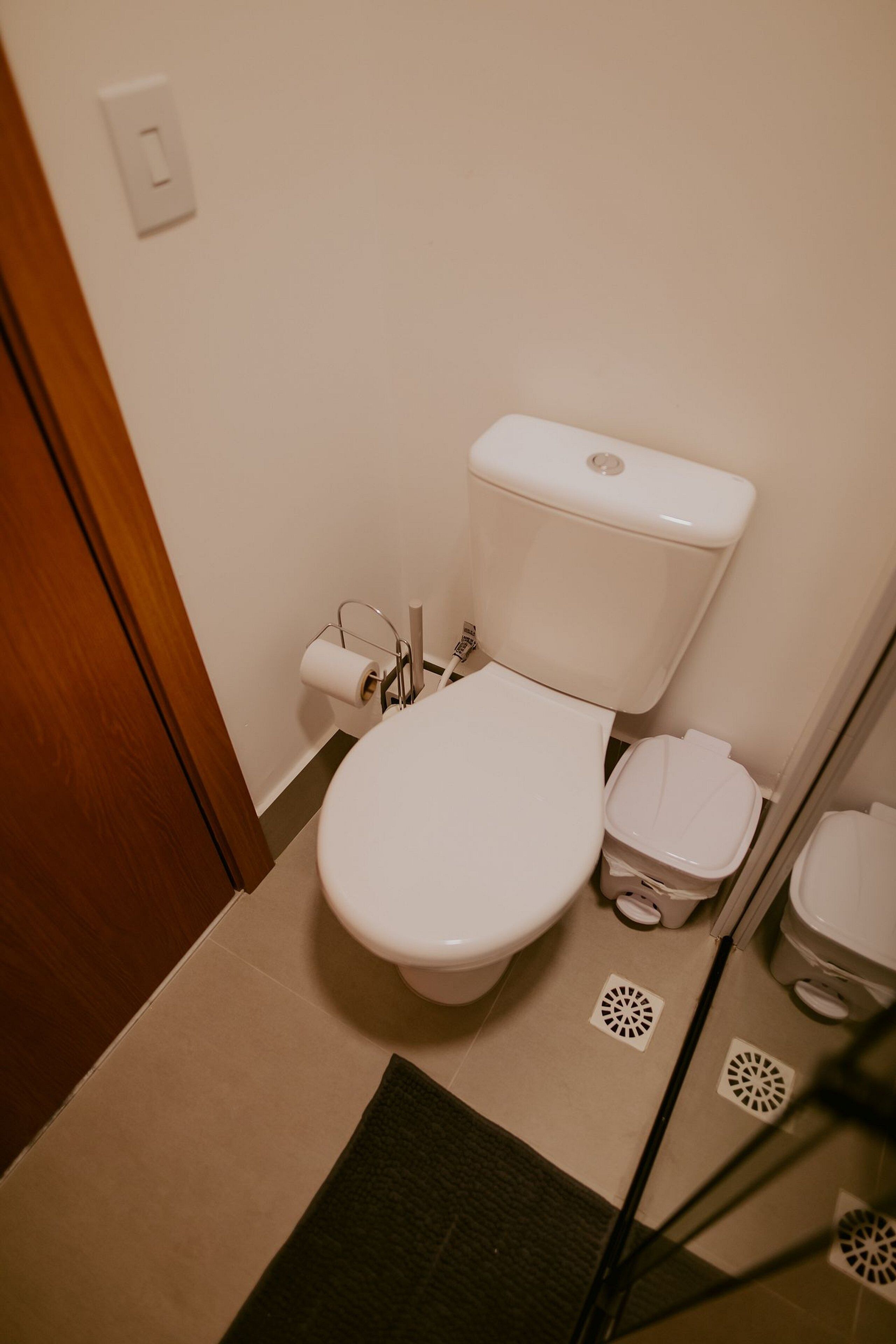 A small bathroom with a toilet, a trash bin, and a toilet paper holder.