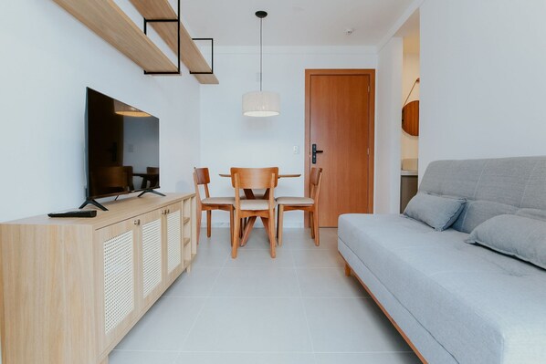 Uma sala de estar moderna com sofá, TV, armário de madeira e mesa de jantar com cadeiras.