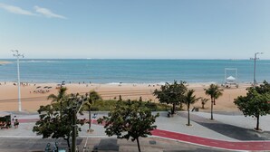 Uitzicht op een strand met een verharde promenade, palmbomen en een heldere lucht.