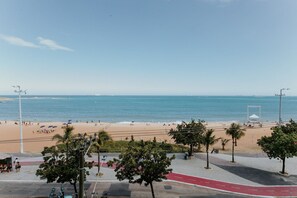 Blick auf einen Strand mit gepflastertem Gehweg, Palmen und blauem Himmel.