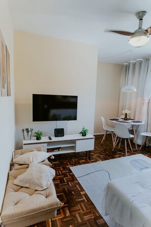 Ein modernes Hotelzimmer mit Flachbildfernseher, einem Esstisch mit Stühlen, einer Couch und einem Deckenventilator.