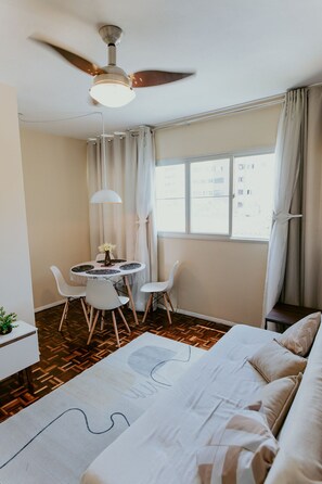 Ein Schlafzimmer mit einem Bett, einem Schreibtisch, Stühlen, einem Deckenventilator und einem Fenster mit Vorhängen.