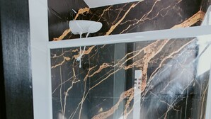 Een badkamer met een douche met glazen wand, een wit toilet en een marmeren wand met een zwart en goud patroon.