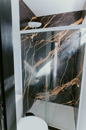 Ein Badezimmer mit einer gläsernen Duschkabine, einer weißen Toilette und einer Marmorwand mit schwarzem und goldenem Muster.