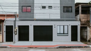 Een gebouw met twee verdiepingen, een garage deur, een klein raam en een zichtbare elektriciteitskast.