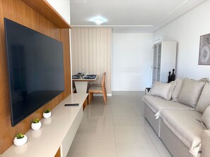 Ein modernes Wohnzimmer mit Flachbildfernseher, einem Esstisch mit Stühlen, einer Couch und einem Schrank.