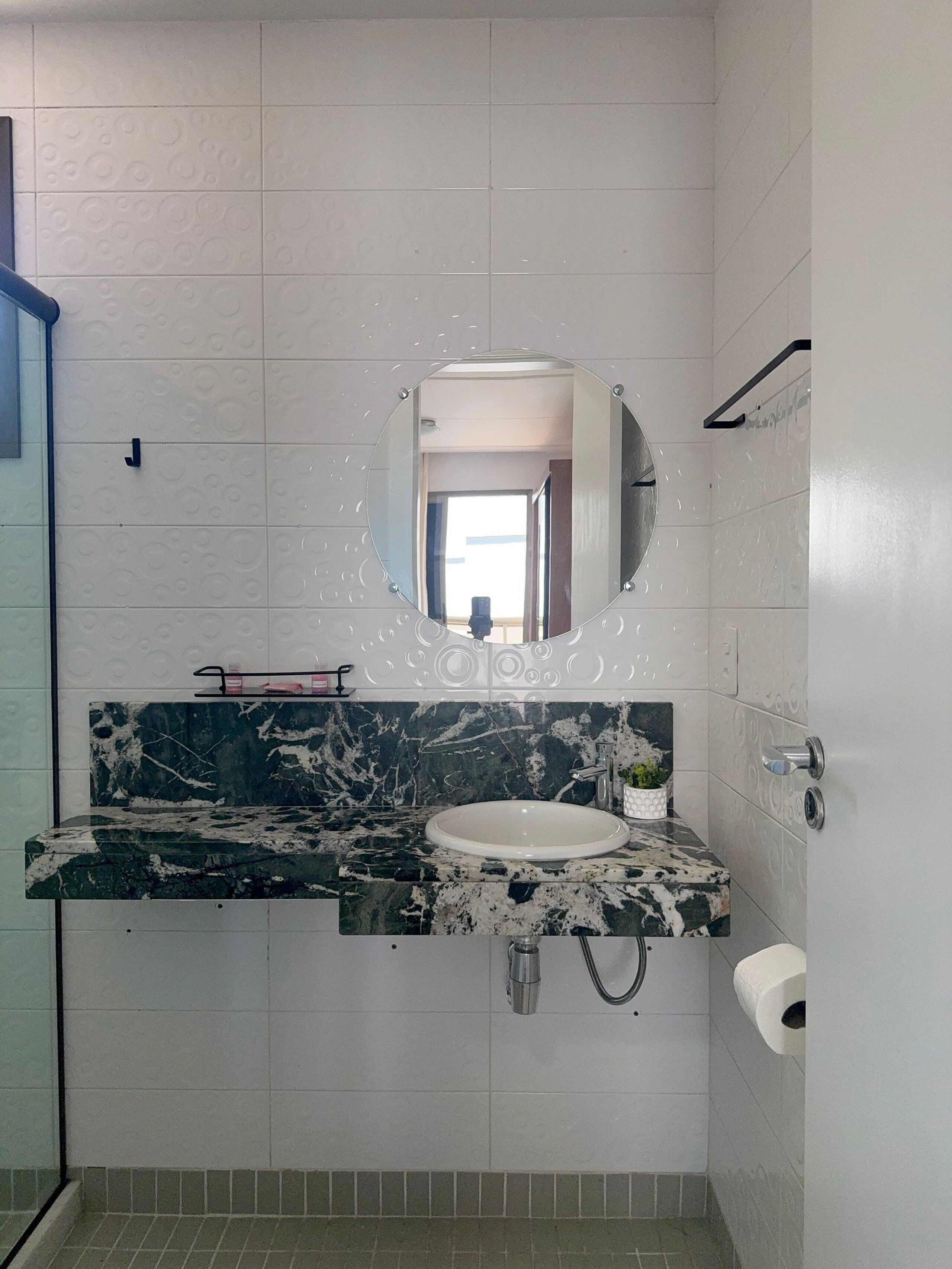 Un bagno con lavandino bianco, uno specchio rotondo, un portascopevoli e un porta carta igienica.