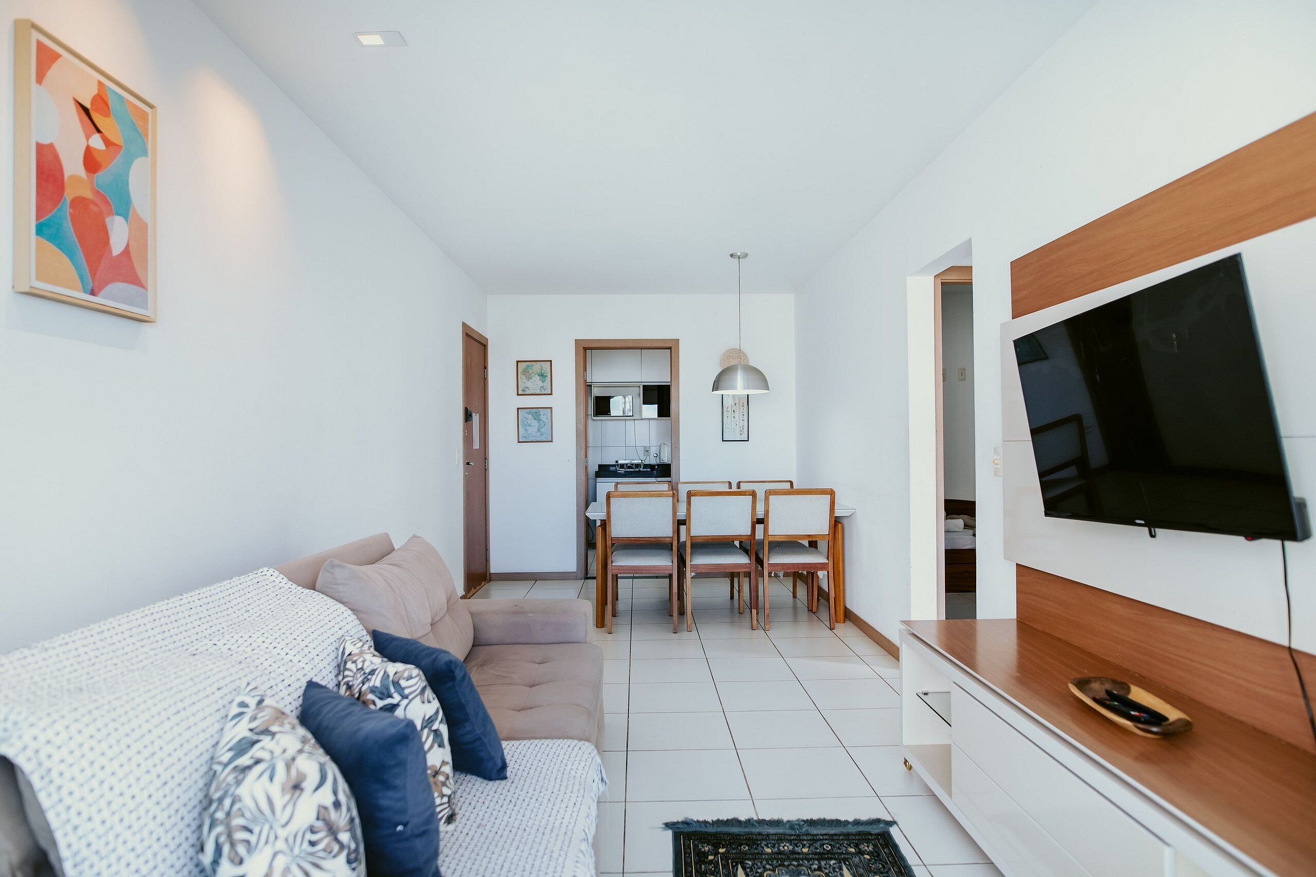 A modern living room with a sofa, TV, dining area, and kitchen in the background.