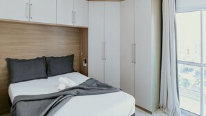 Camera da letto con un letto, una testiera in legno, armadietti bianchi e un'ampia finestra con tende.