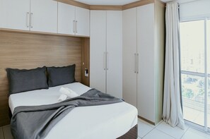 Ein Schlafzimmer mit Bett, Holz-Kopfteil, weißen Schränken und einem großen Fenster mit Vorhängen.