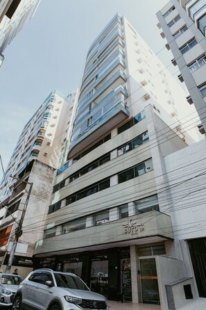 A multi-story building with a modern architectural design, featuring a prominent entrance with signage. - 2-bedroom apartment with the best location in Guarapari. (Guarapari)