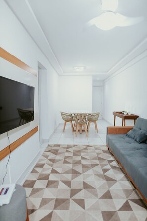 A modern living room with a flat-screen TV, a sofa, a dining table with chairs, and a patterned floor. - 2-bedroom apartment with the best location in Guarapari. (Guarapari)