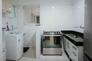 A compact kitchen with a washing machine, a stove, and a sink. - 2-bedroom apartment with the best location in Guarapari. (Guarapari)