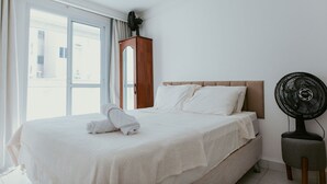 Een hotelkamer met een bed, een houten nachtkastje, een ventilator en een raam met gordijnen.