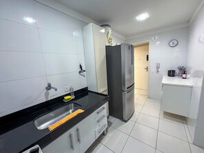 Una cocina moderna con azulejos blancos, un refrigerador de acero inoxidable, una encimera negra y un lavamanos.