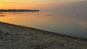 Ein Strand mit ruhiger See, weiter Küste und blauem Himmel.