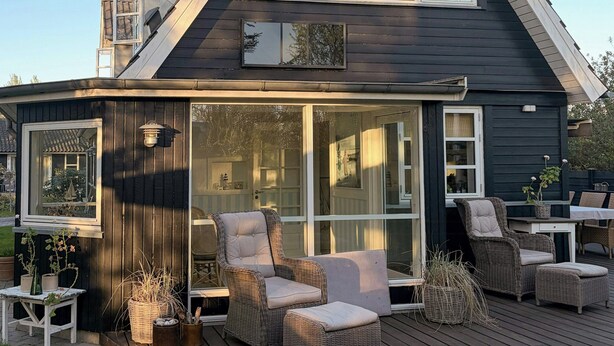 Ein Haus mit einer großen Terrasse, Sitzgelegenheiten im Freien und einem auffälligen Fenster.