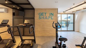 Un gimnasio con cintas de correr, una elíptica y una bicicleta estática. Hay una pared con la frase 'GET IN SHAPE'.