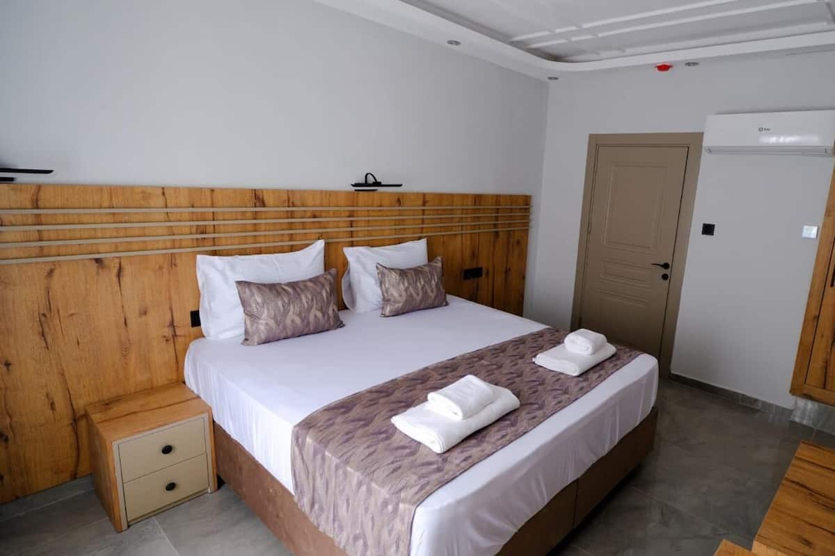 Ein Hotelzimmer mit einem hölzernen Kopfteil, einem Bett mit weißer Bettwäsche, einem Nachttisch aus Holz und einem Kleiderschrank.