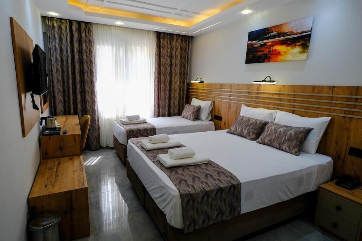 A hotel room with two beds, a desk, a chair, a TV, and a painting on the wall.
