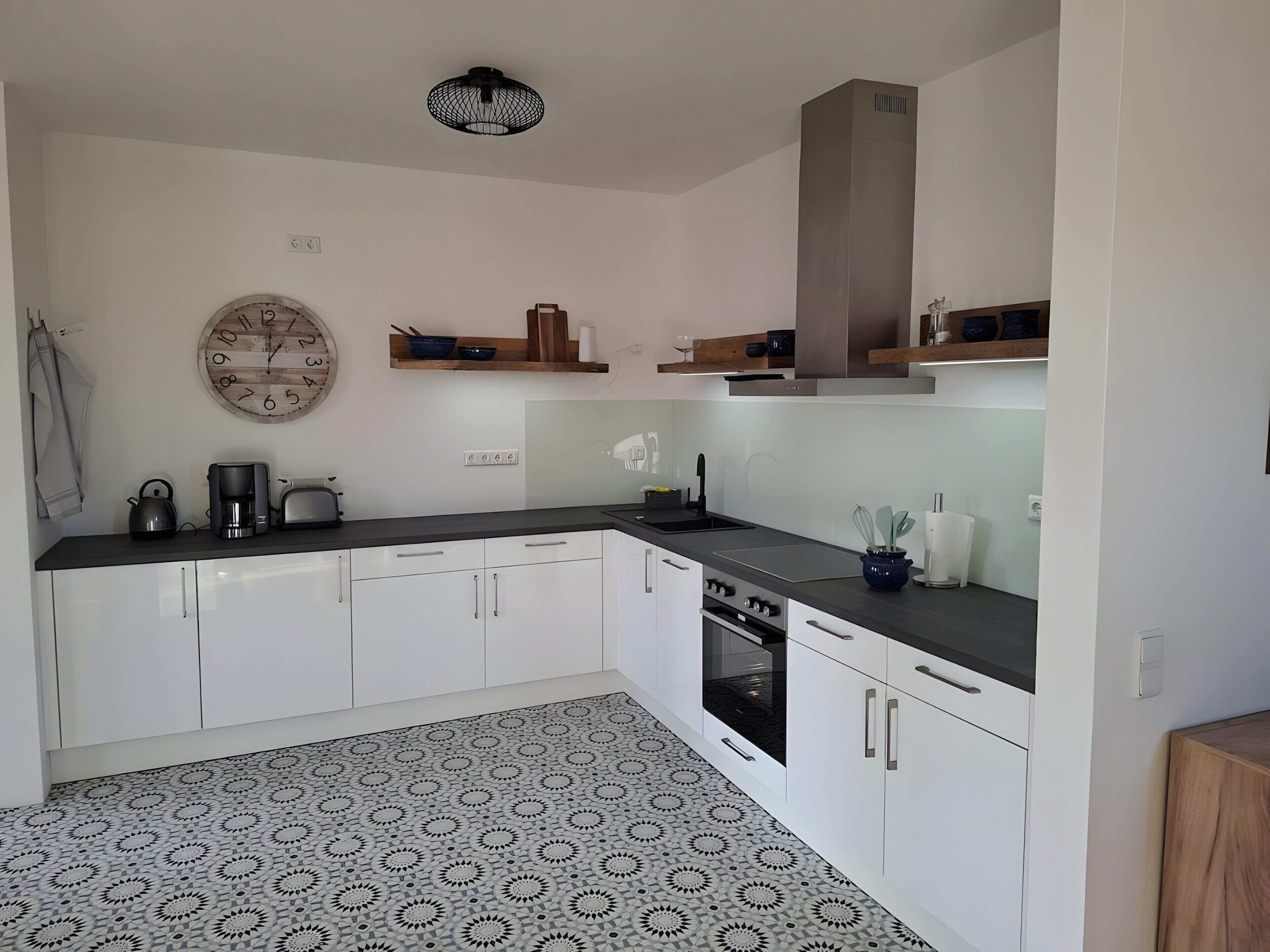 A modern kitchen with white cabinets, a black countertop, a patterned floor, and a clock on the wall.