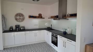 Una cocina moderna con armarios blancos, encimera negra, suelo estampado y un reloj en la pared.