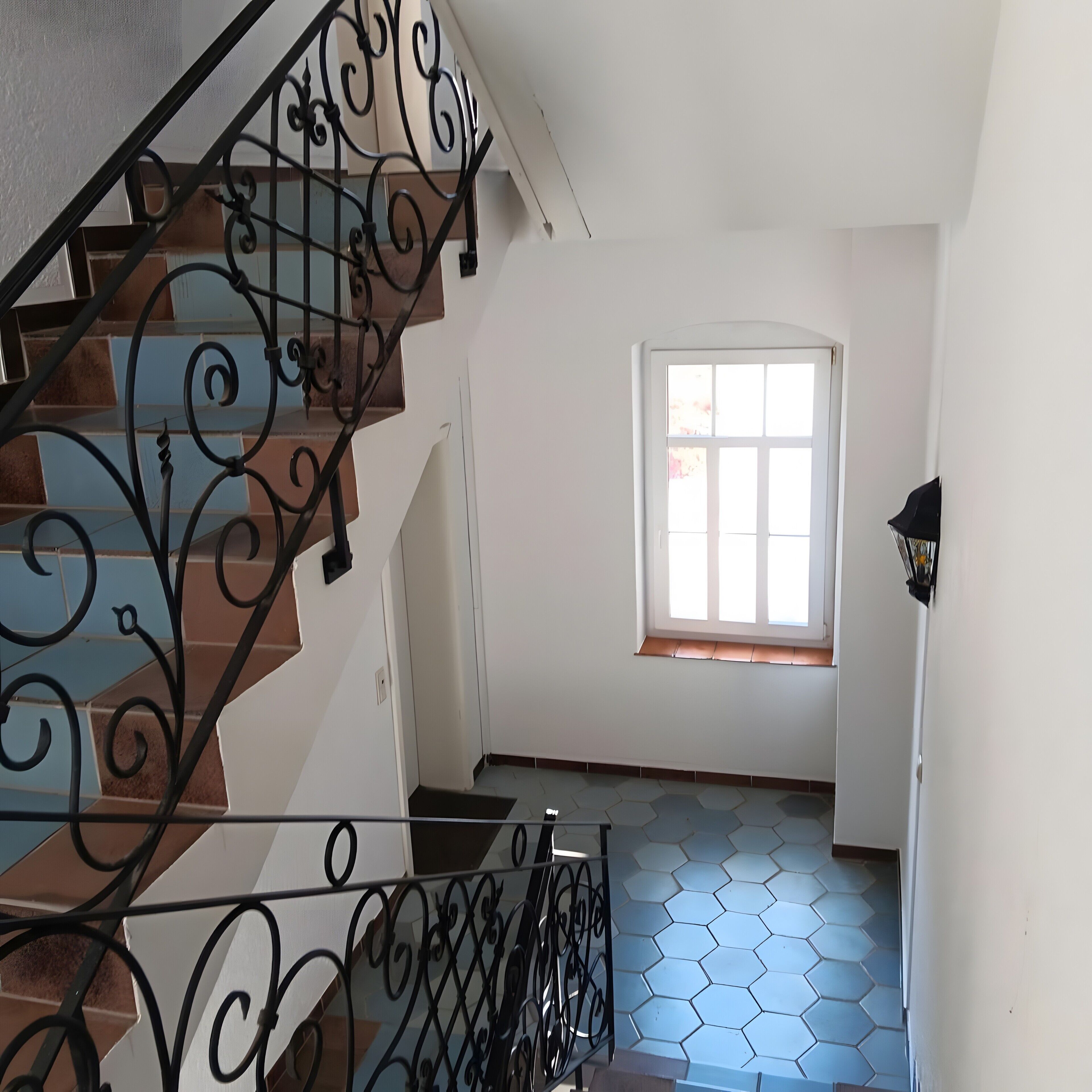 Una escalera con barandillas de metal decoradas, un ventanal con vistas y un suelo de baldosas.