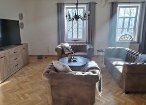 Ein Wohnzimmer mit einer Couch, einem Couchtisch, einem Fernseher auf einem Schrank und einer Deckenleuchte.