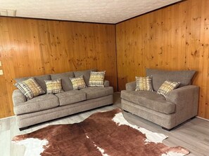 Une pièce avec deux canapés gris, un tapis marron et blanc, et des murs recouverts de panneaux en bois.