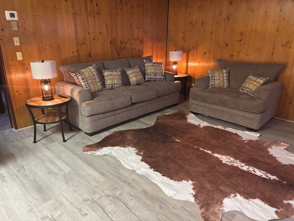 Un salon comprenant deux canapés, une table ronde en bois, un tapis en peau de vache et deux lampes de table.