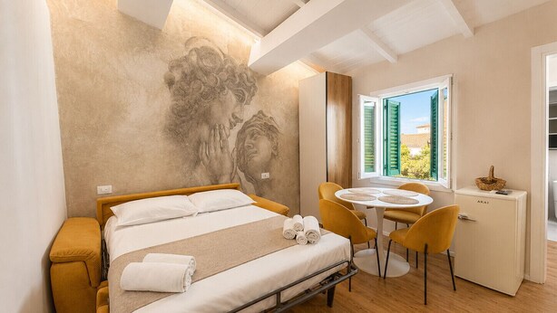 A bedroom with a bed, a desk, chairs, a window with shutters, and a wall mural.