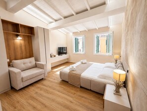 A modern hotel room with a sofa, a bed, a TV, and a window with shutters. - Pitti Prestige Suites 2 (Florence)
