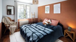 Ein Schlafzimmer mit Bett, Stuhl, einer Leiter, einem Heizkörper und Bildern an den Wänden.