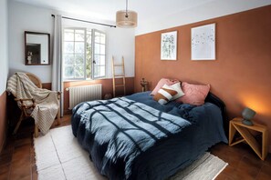 Ein Schlafzimmer mit Bett, Stuhl, einer Leiter, einem Heizkörper und Bildern an den Wänden.