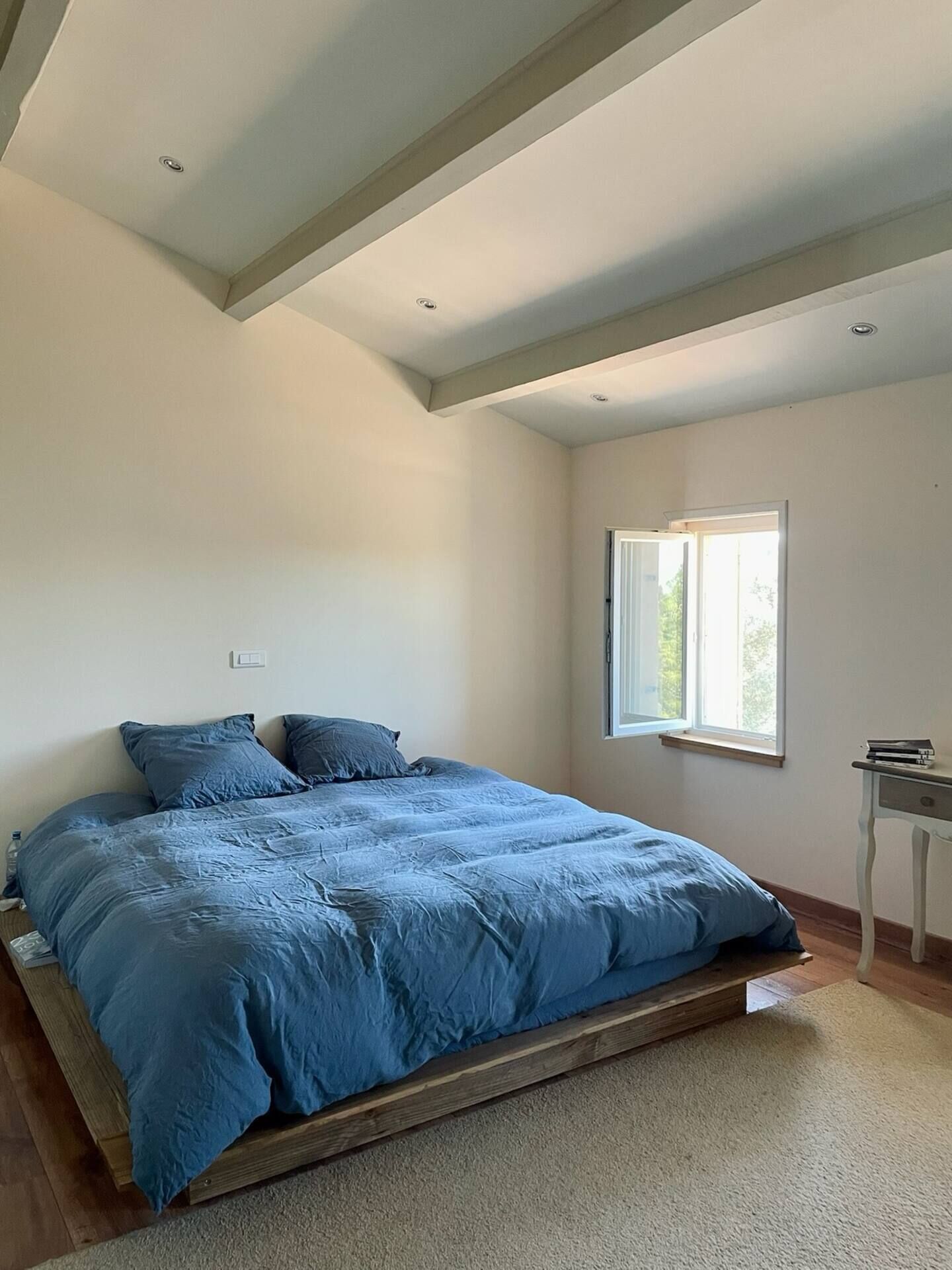 Une chambre avec un grand lit, une fenêtre et une petite table.