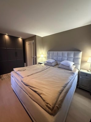 Une chambre à coucher avec un grand lit, une armoire, une table de chevet avec une lampe et une porte.
