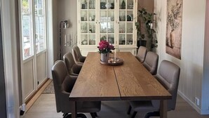 Een eetkamer met een houten tafel, zes stoelen, een kast met glazen deuren en een schilderij aan de muur.