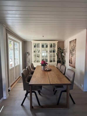 Uma sala de jantar com uma mesa de madeira, seis cadeiras, um aparador com portas de vidro e um quadro na parede.