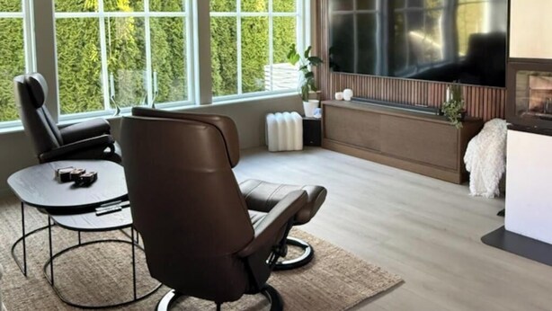 Een moderne woonkamer met een grote televisie, comfortabele zithoek en grote ramen.