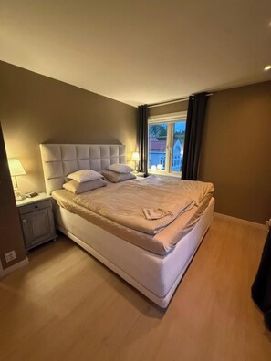 Quarto com uma cama grande, mesa de cabeceira, abajur e vista para o exterior.