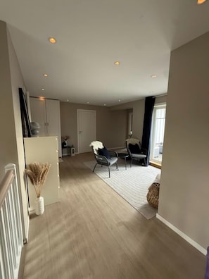 Une pièce spacieuse avec un plafond haut, un plancher en bois et un coin salon avec deux fauteuils.
