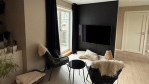 Een moderne woonkamer met een flatscreen televisie, zwart-wit meubels, een groot raam en een deur.