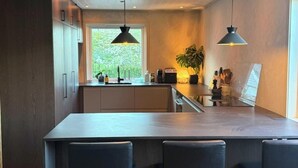 Een moderne keuken met een centraal eiland, hanglampen en uitzicht op groen.